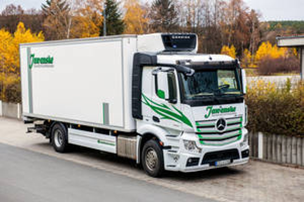 Weißer Mercedes-Benz LKW mit "Juraschek" Aufschrift und grünem Logo parkt auf einem asphaltierten Weg.